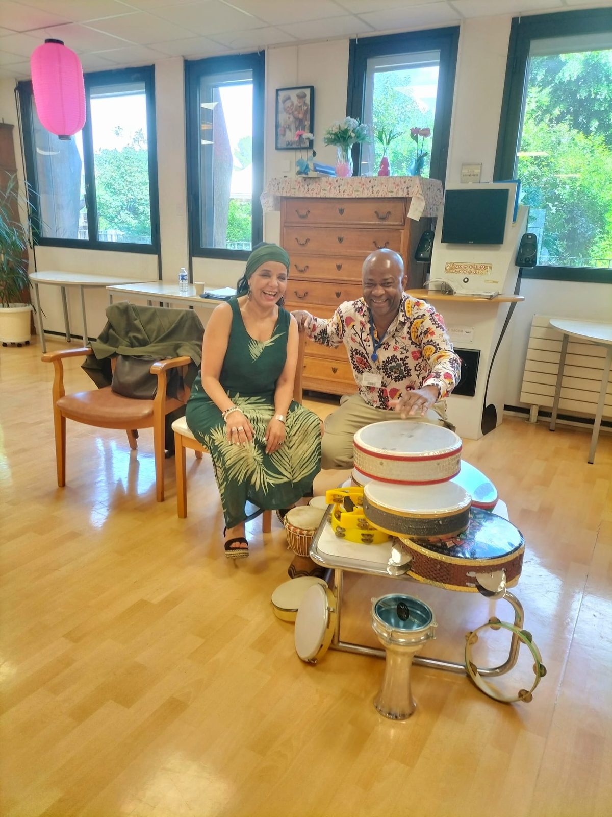 Deux intervenants souriants à côté du chariot de percussions dans la salle commune d'une résidence seniors